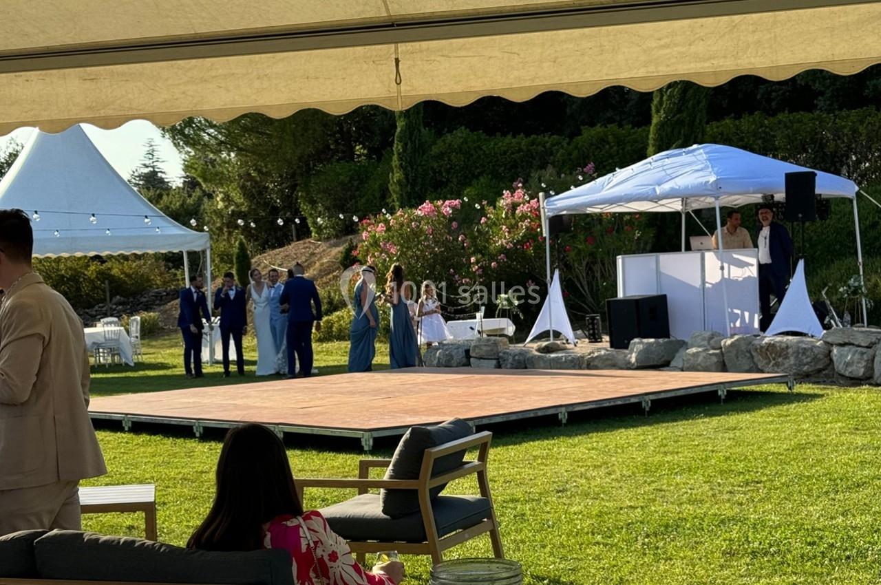 Des personnes rassemblées près d'une piste de danse en plein air, entourée de tentes blanches et de verdure.