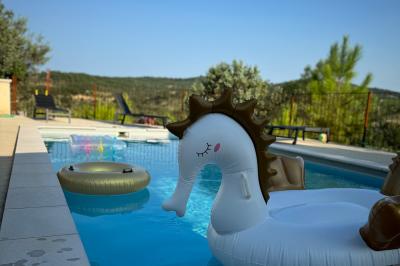Vue d'une table avec croissants et fruits, devant une porte ouverte sur une terrasse avec piscine et paysage verdoyant.