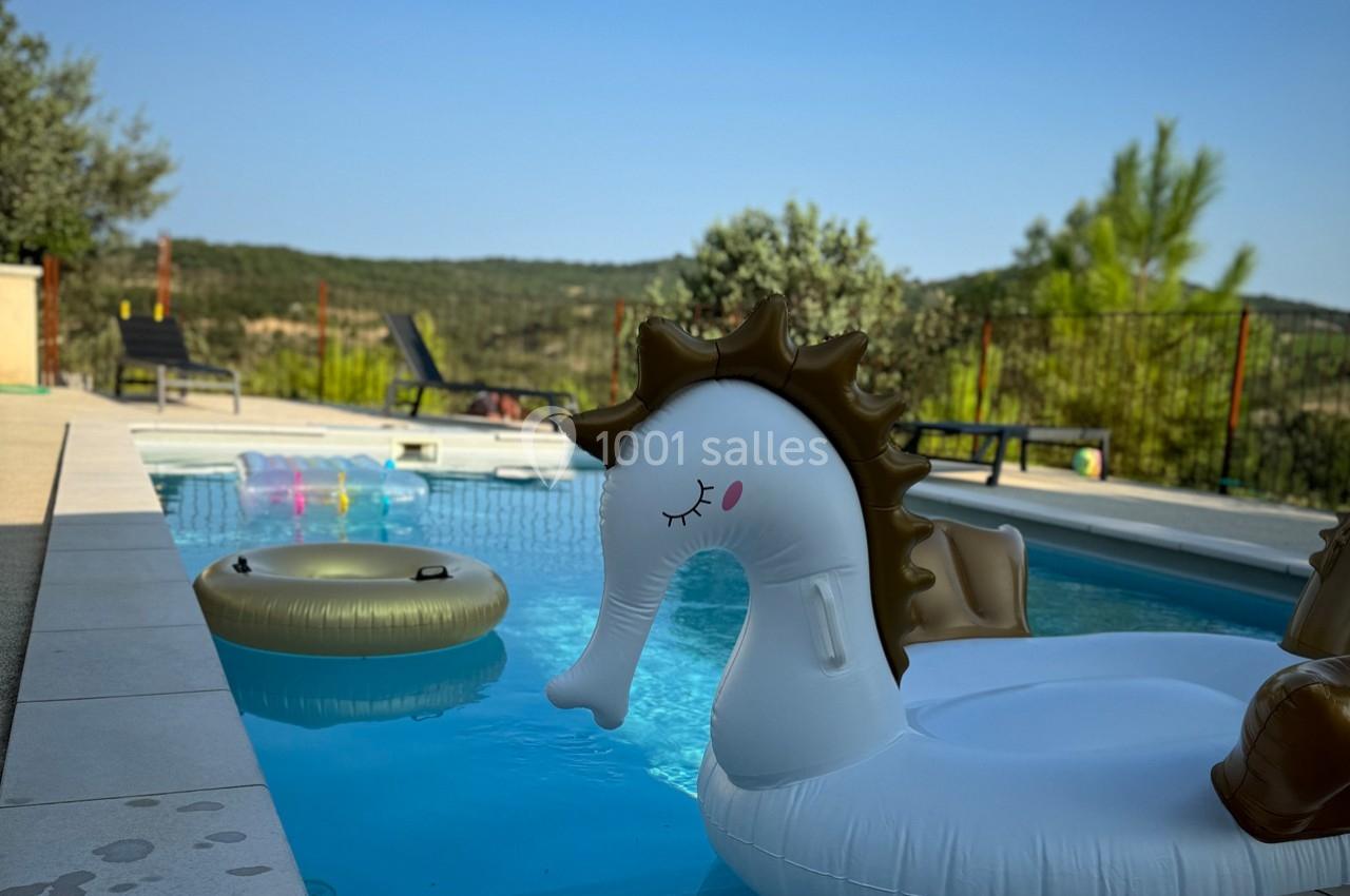Bouée licorne blanche et dorée flottant dans une piscine entourée de végétation et de collines en arrière-plan.