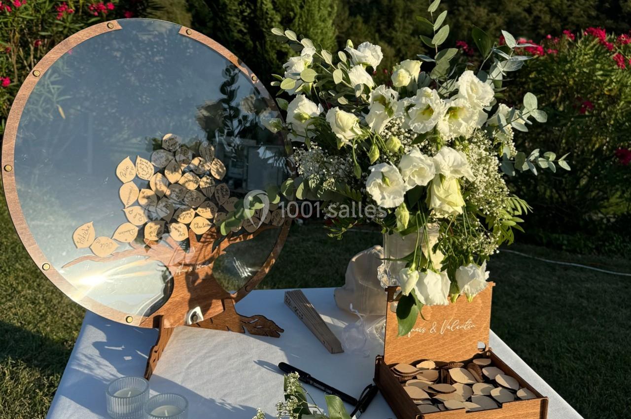Arbre à vœux en bois avec feuilles gravées, bouquet de fleurs blanches et accessoires sur une table en extérieur.