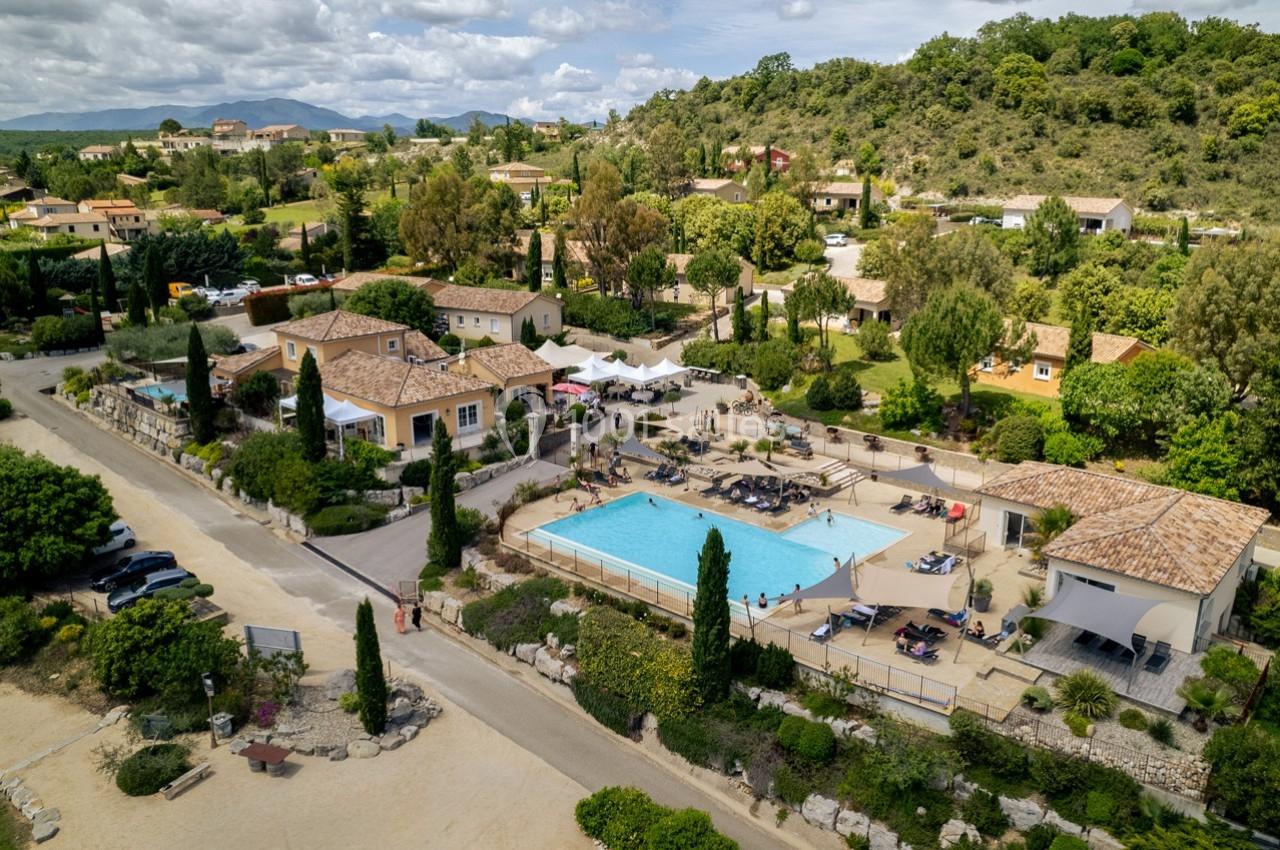 Vue aérienne d'un complexe résidentiel avec piscine, terrasses, végétation et collines en arrière-plan.