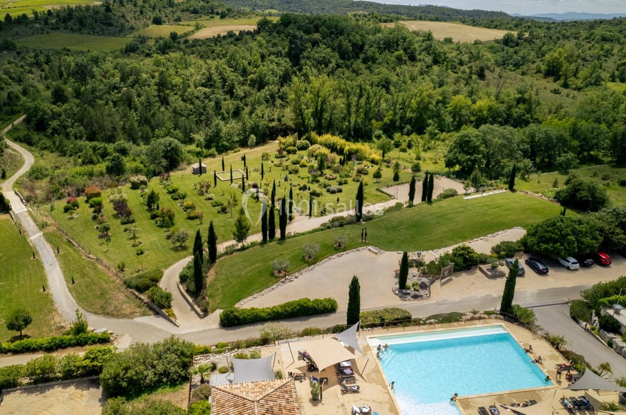 Vue aérienne d'un domaine avec piscine, jardins arborés, allées sinueuses et collines verdoyantes en arrière-plan.