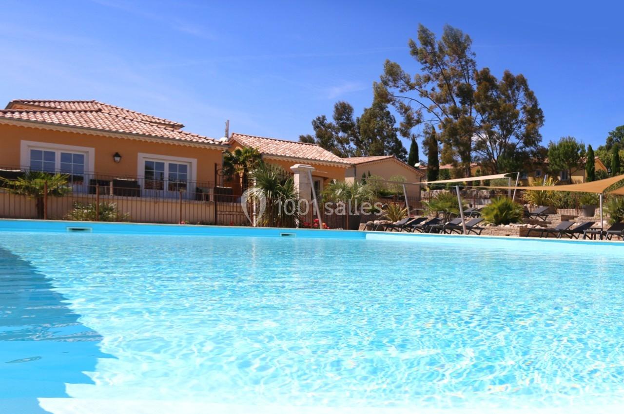 Piscine extérieure avec eau claire devant une maison aux tuiles orangées, entourée de végétation et d'arbres.