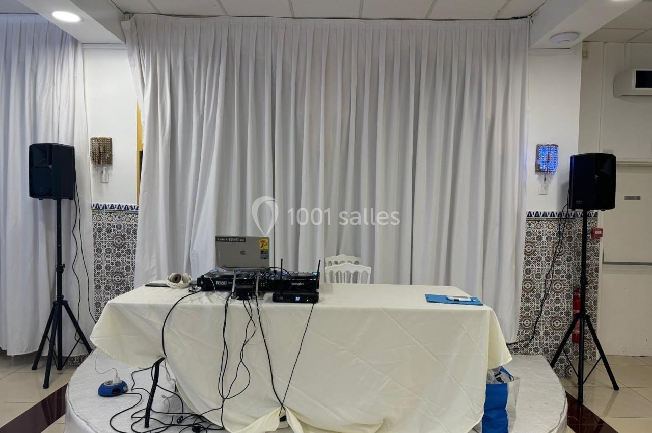 Table équipée de matériel de sonorisation avec câbles, ordinateur et enceintes, devant un rideau blanc.