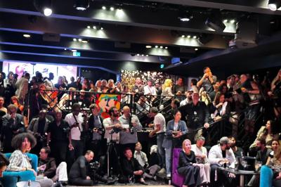 Un homme et une femme posent ensemble dans un environnement sombre, la femme tenant un verre à la main.