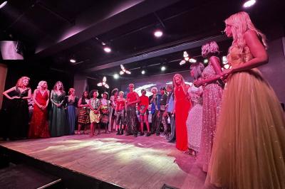 Un homme et une femme posent ensemble dans un environnement sombre, la femme tenant un verre à la main.