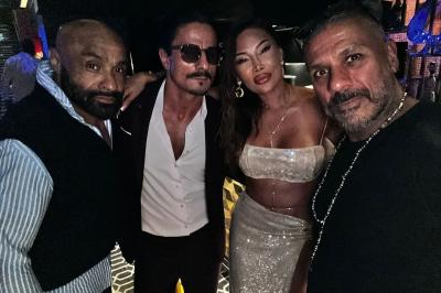 Un homme et une femme posent ensemble dans un environnement sombre, la femme tenant un verre à la main.