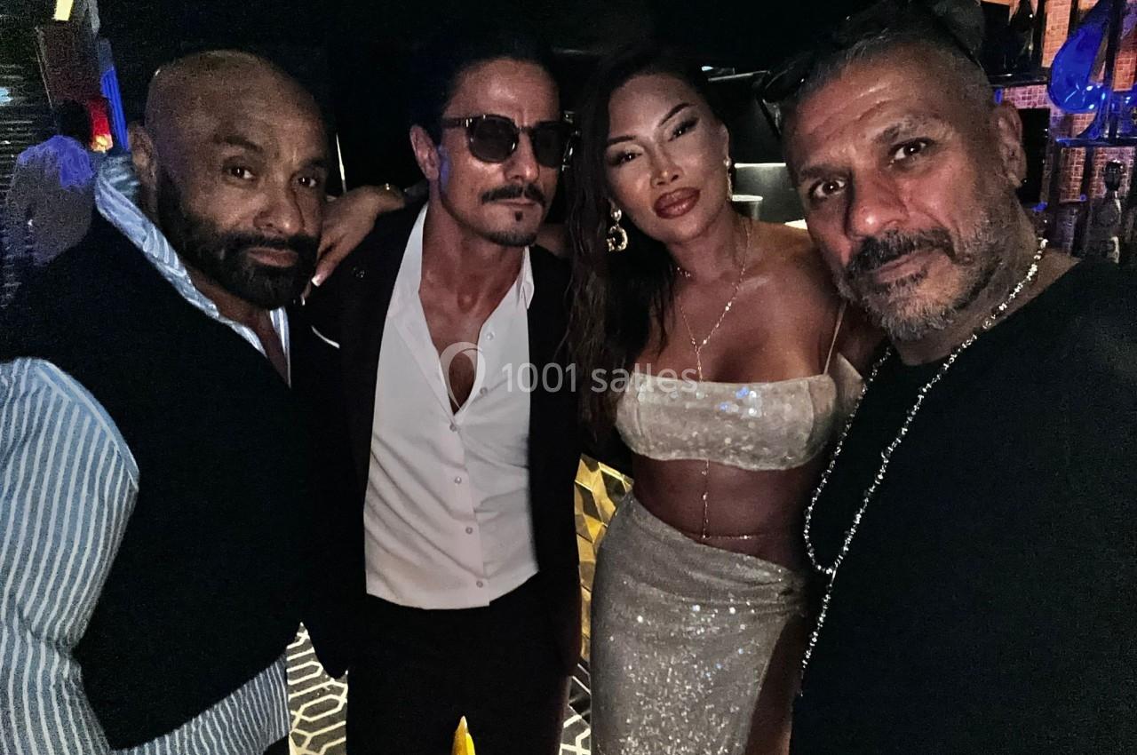 Quatre personnes posent ensemble dans un environnement sombre, vêtues de tenues élégantes et festives.