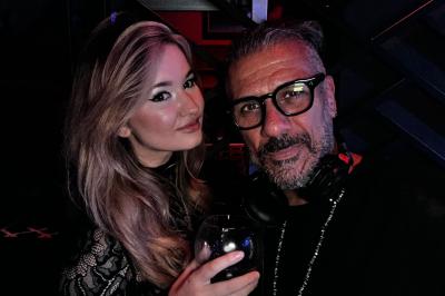 Un homme et une femme posent ensemble dans un environnement sombre, la femme tenant un verre à la main.