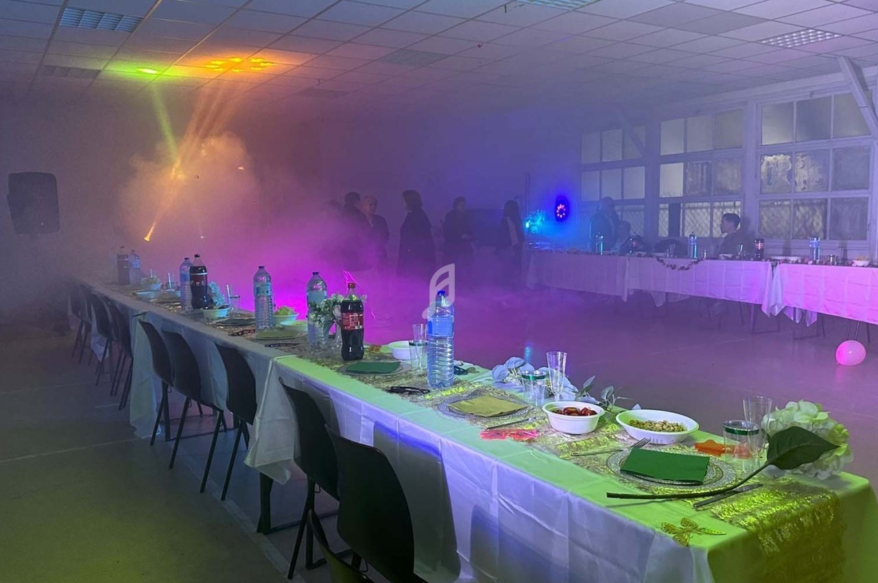 Salle décorée pour un événement avec tables dressées, éclairage coloré et ambiance enfumée.