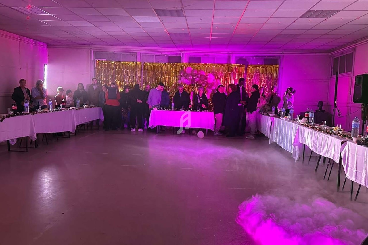 Salle décorée pour une fête avec des invités debout près d'une table centrale, éclairage rose et fumée au sol.