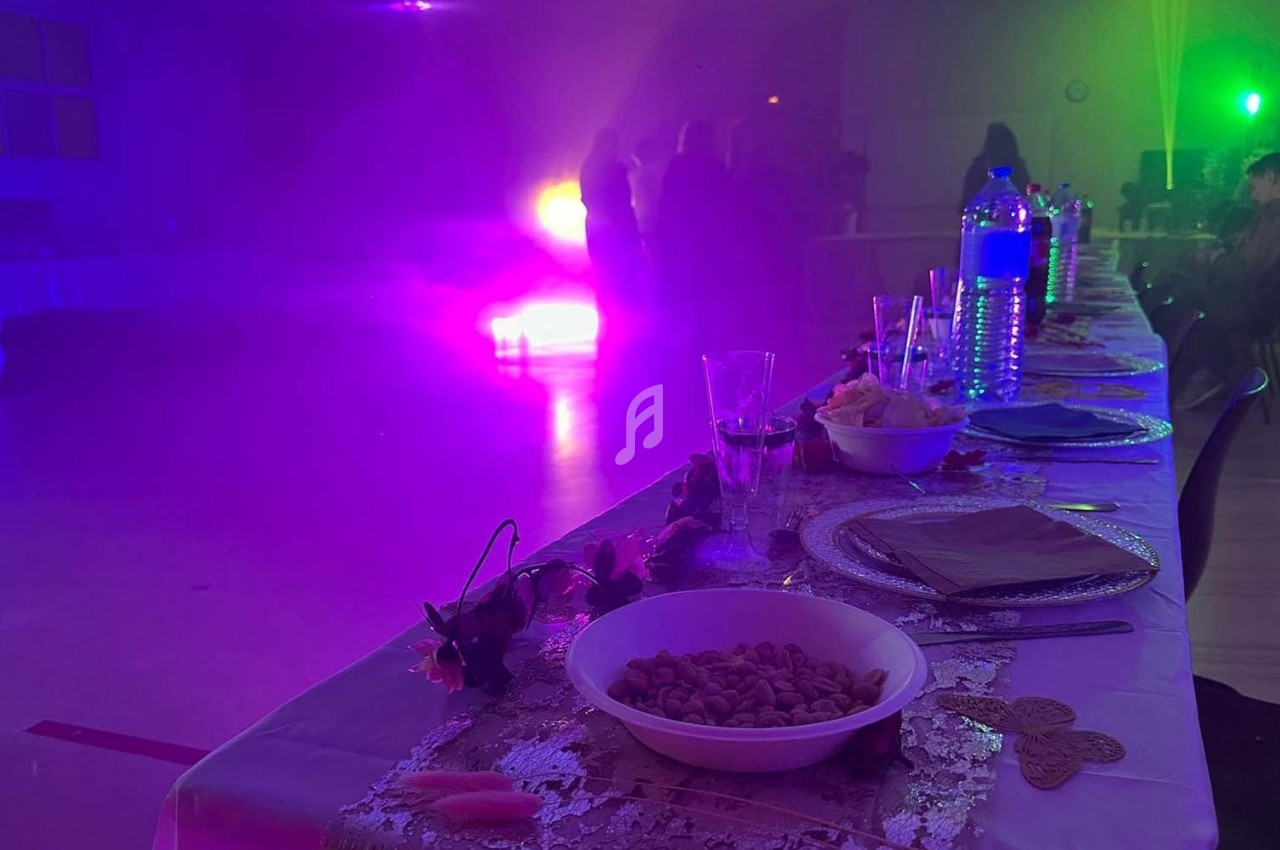 Table dressée avec des assiettes, verres et snacks, dans une salle éclairée par des lumières colorées et une ambiance…