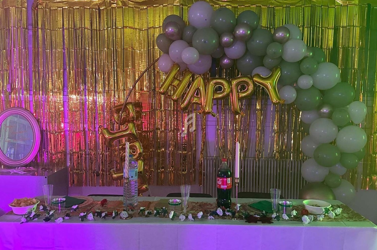 Décoration de fête avec ballons verts et dorés, guirlandes dorées et table dressée avec boissons et snacks.