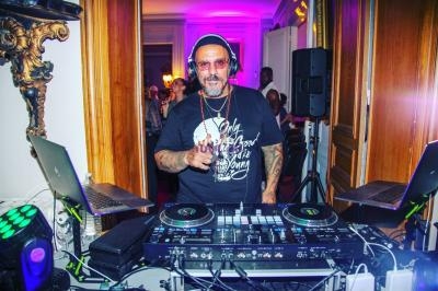 Un DJ portant un casque anime une soirée dans une pièce éclairée par des lumières colorées, entouré de matériel audio.