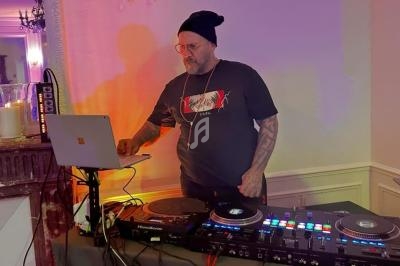 Un DJ portant un bonnet mixe de la musique sur une console, avec un ordinateur portable à ses côtés dans une pièce éclairée.