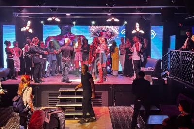 Un groupe de personnes rassemblé sur une scène et autour, dans un espace intérieur avec éclairage coloré.