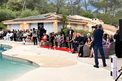 Un photographe capture un événement en plein air près d'une piscine, avec des invités assis et un tapis rouge.