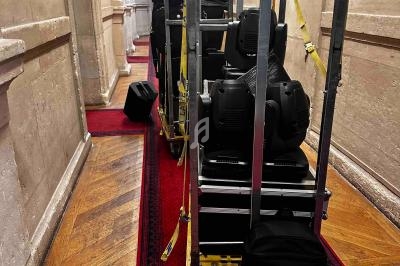 Chariot chargé de matériel technique sur un tapis rouge dans un couloir aux murs en pierre.