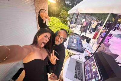 Une femme et un DJ posent joyeusement près d'une table de mixage lors d'un événement en extérieur.