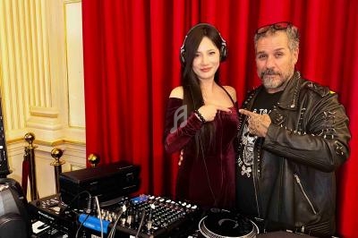 Une femme et un homme posent devant une table de mixage, avec un rideau rouge en arrière-plan.
