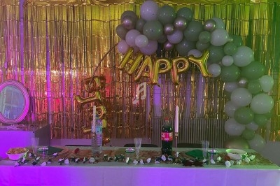 Décoration de fête avec ballons verts et dorés, guirlande ’Happy’, table dressée avec boissons et snacks.