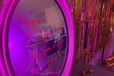 Texte alt : Miroir décoré avec l'inscription ’Joyeux Anniversaire, Vive tes 60 ans’ reflétant une table de fête et des…