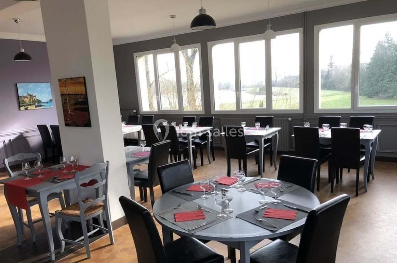Salle de restaurant lumineuse avec tables dressées, chaises noires et vue sur un paysage extérieur verdoyant.