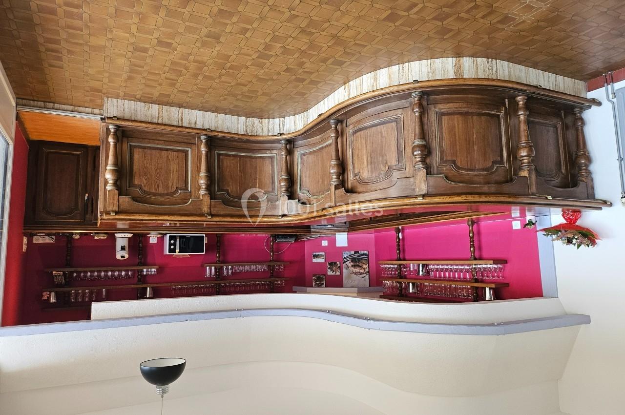 Comptoir de bar blanc avec étagères en bois sculpté, murs roses et plafond à motif doré.