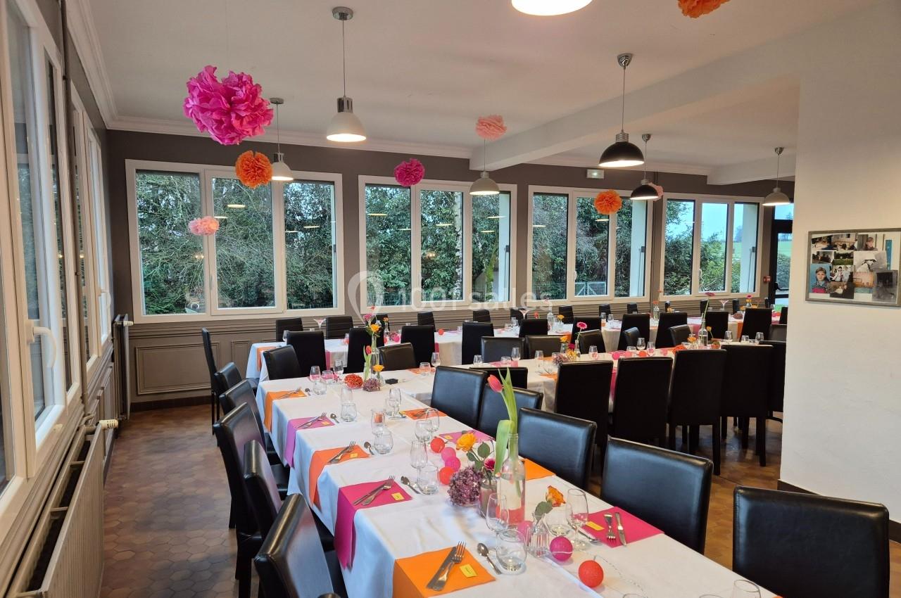 Salle de réception lumineuse avec tables dressées, nappes blanches et décorations colorées suspendues.
