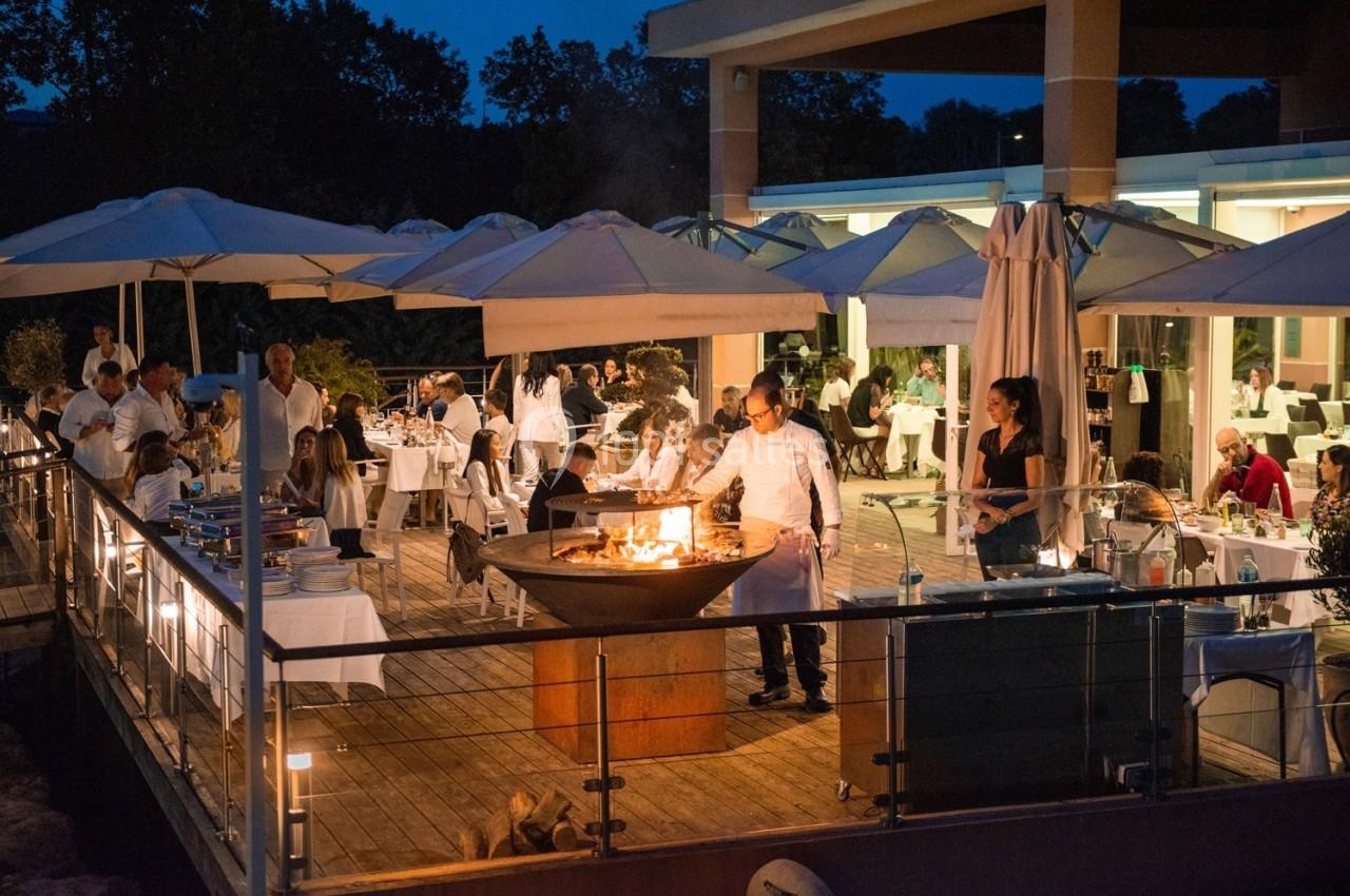 Terrasse d'un restaurant en soirée avec des convives attablés et un chef cuisinant sur un brasero.