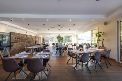 Salle de restaurant lumineuse avec tables rondes dressées, chaises marron et grandes baies vitrées.