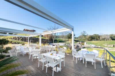 Salle de restaurant lumineuse avec tables rondes dressées, chaises marron et grandes baies vitrées.