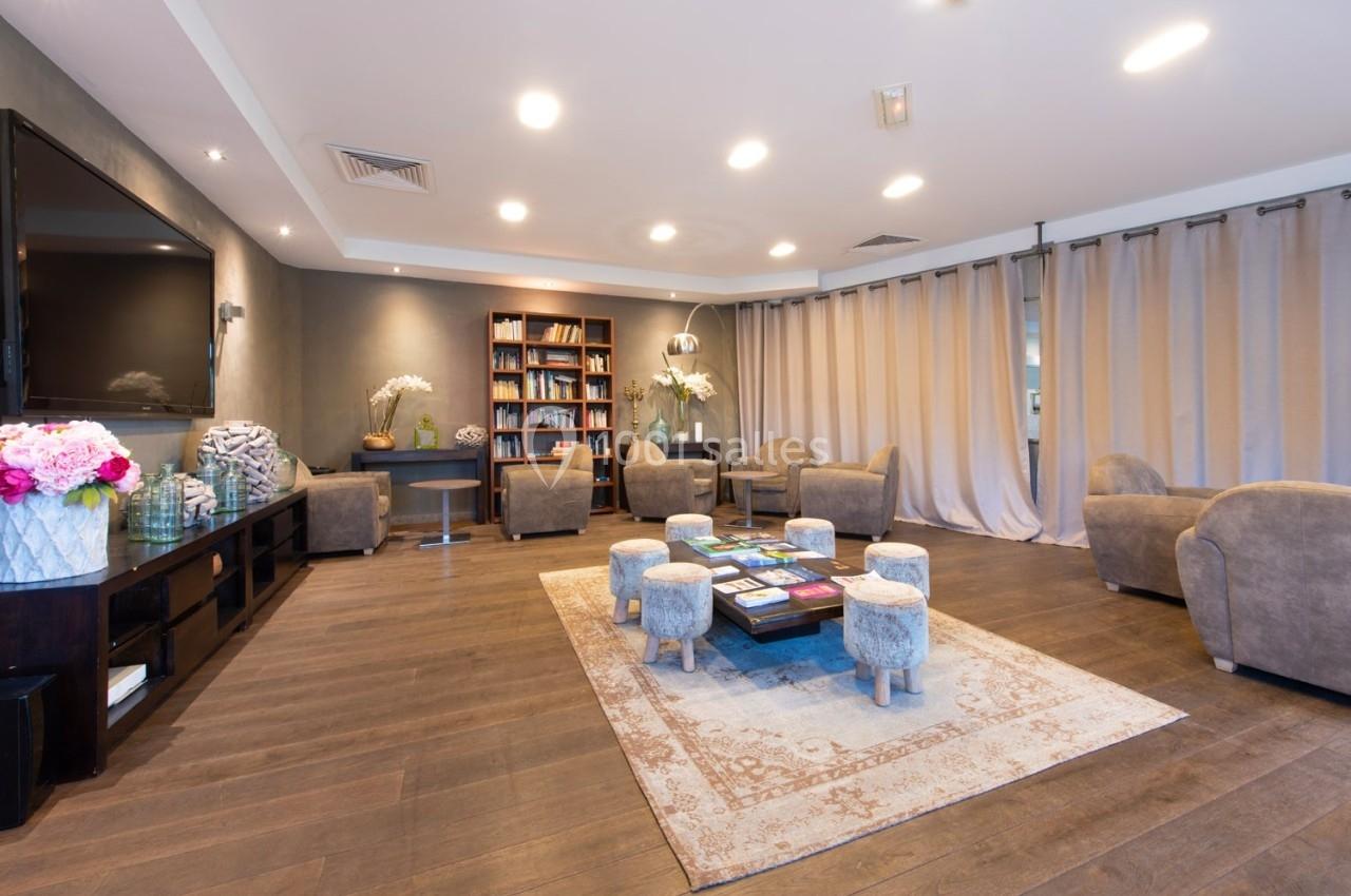 Salon spacieux avec fauteuils, bibliothèque, tapis décoratif et éclairage chaleureux, ambiance conviviale et moderne.