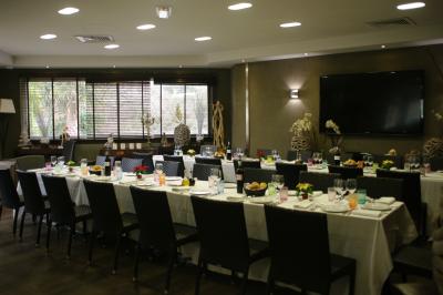 Salle de restaurant lumineuse avec tables rondes dressées, chaises marron et grandes baies vitrées.