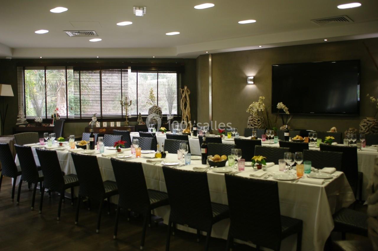 Salle de réception avec de longues tables dressées pour un repas, éclairée par des fenêtres et des luminaires modernes.