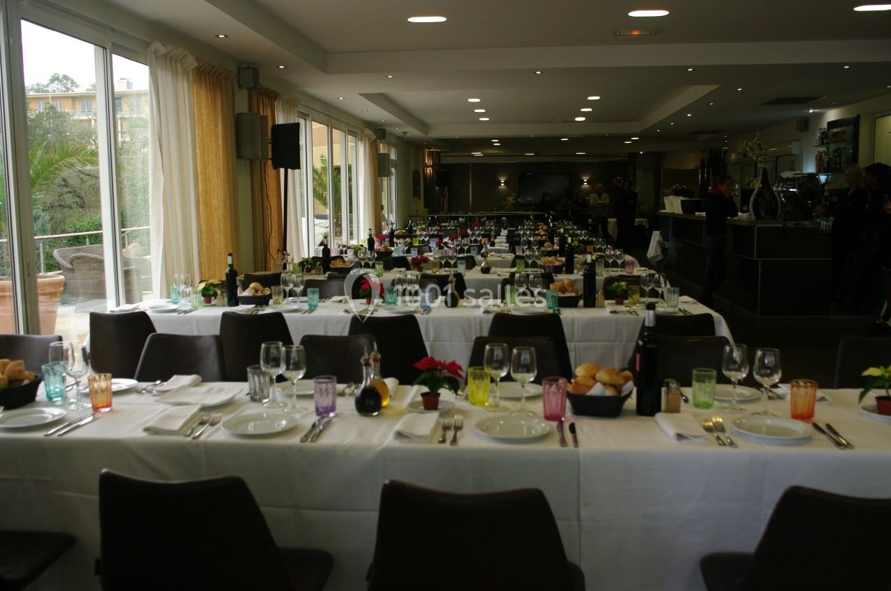 Salle de réception avec de longues tables dressées pour un repas, décorées de fleurs et de vaisselle colorée.