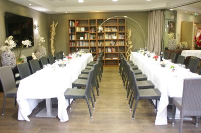 Salle de restaurant lumineuse avec tables rondes dressées, chaises marron et grandes baies vitrées.