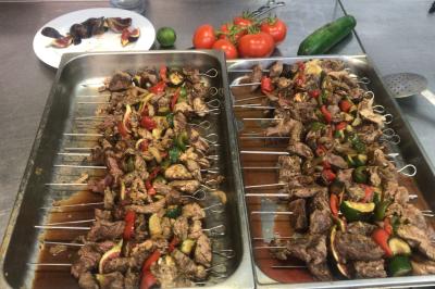 Brochettes de viande et légumes colorés disposées sur des plateaux en cuisine, avec des légumes frais en arrière-plan.