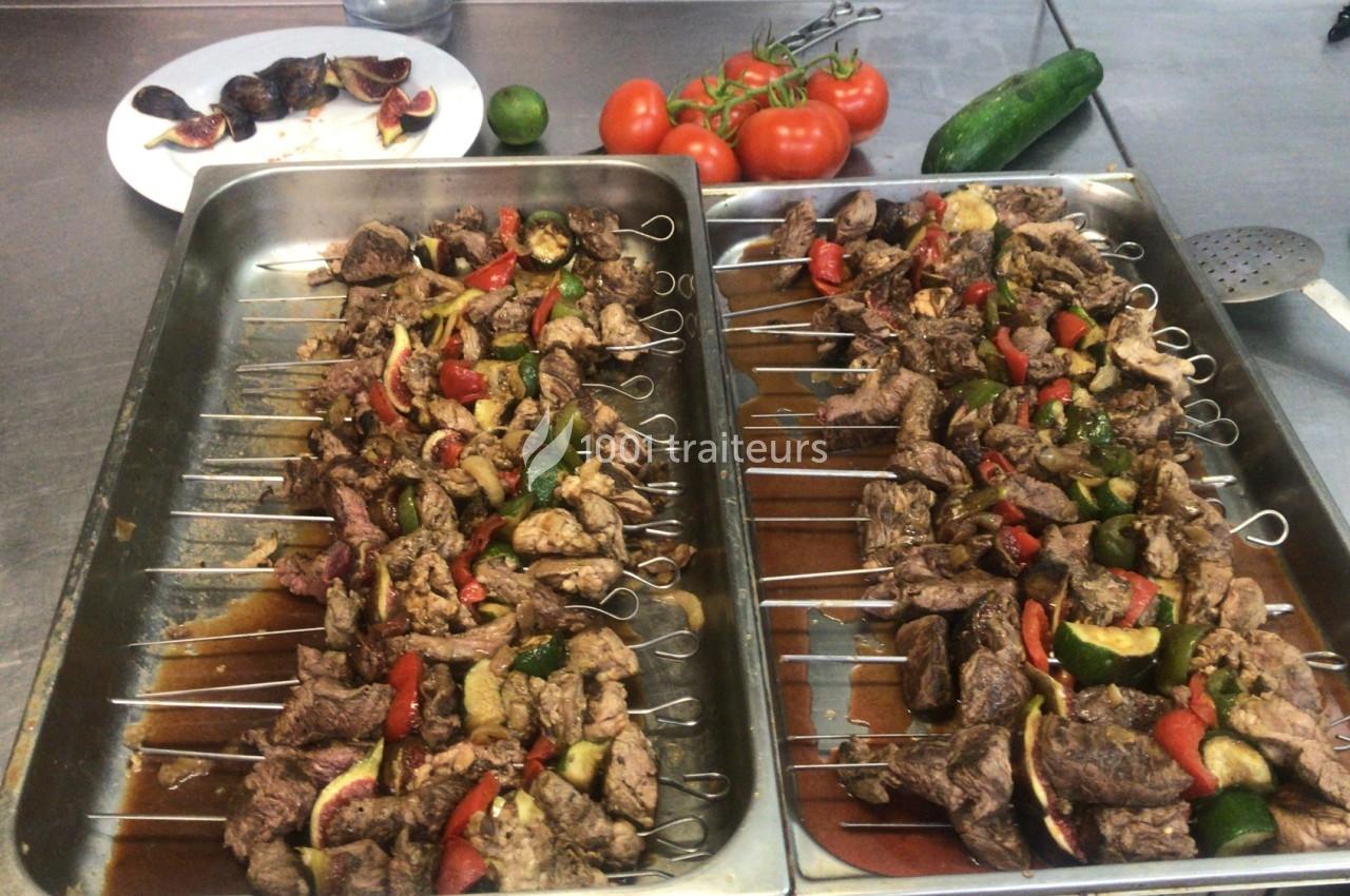 Brochettes de viande et légumes colorés disposées sur des plateaux en cuisine, avec des légumes frais en arrière-plan.