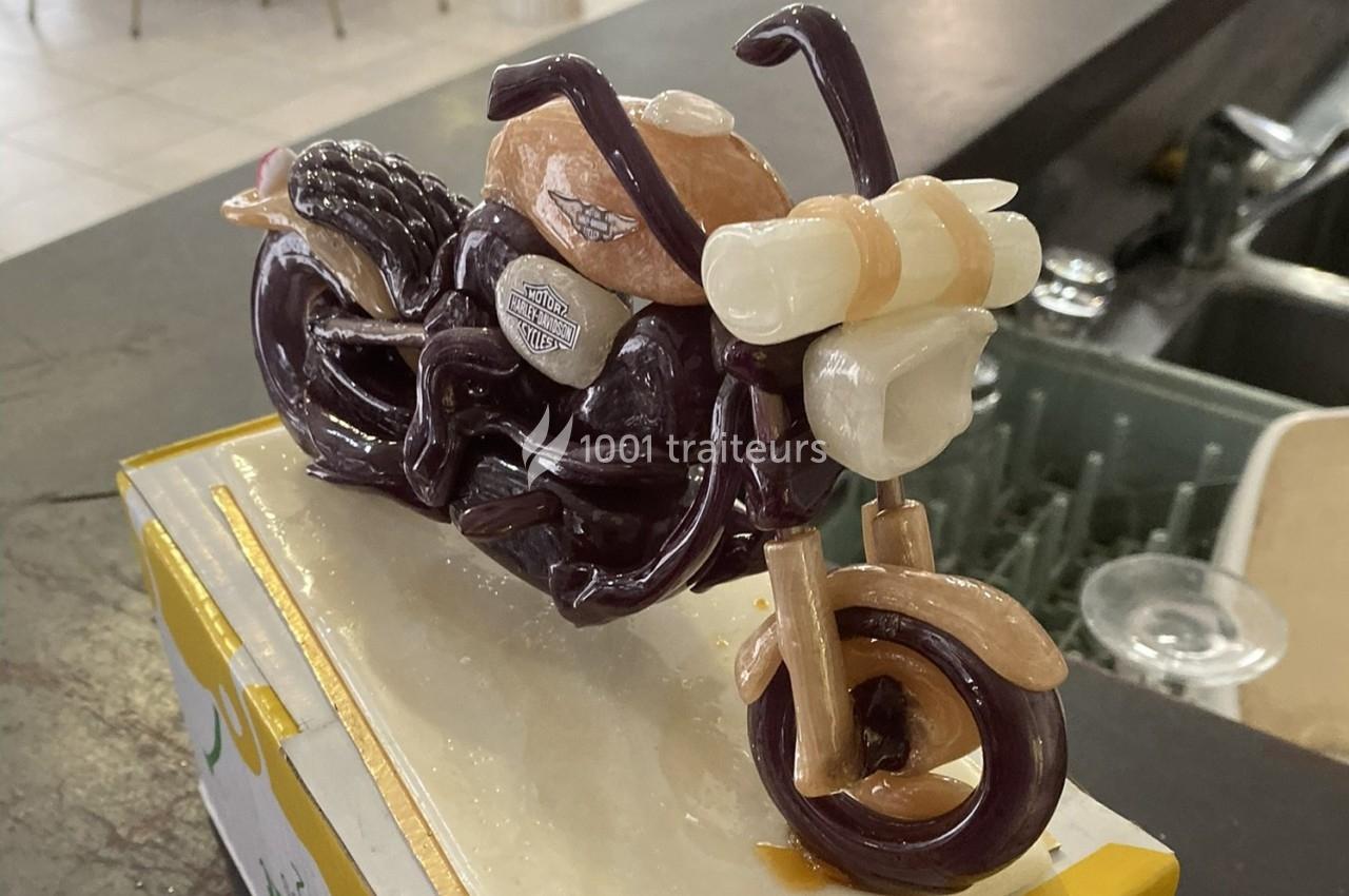 Sculpture miniature d'une moto réalisée en matériaux comestibles, posée sur une surface blanche.