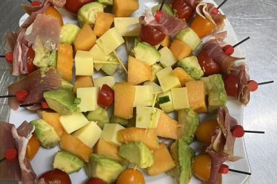 Brochettes de viande et légumes colorés disposées sur des plateaux en cuisine, avec des légumes frais en arrière-plan.