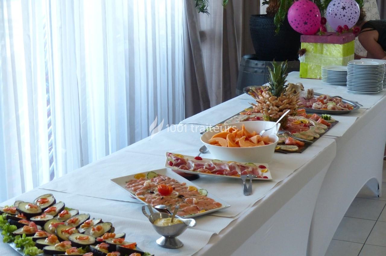 Buffet avec divers plats froids, dont des fruits, des légumes et des charcuteries, disposés sur une table blanche.