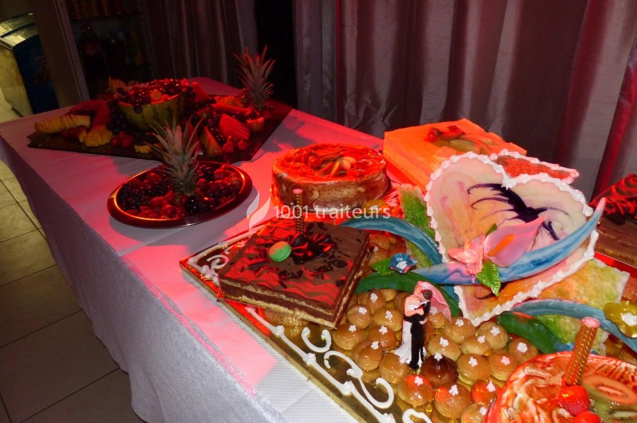 Table garnie de desserts variés, dont des gâteaux décorés, des fruits et des pâtisseries, éclairée par une lumière rouge.