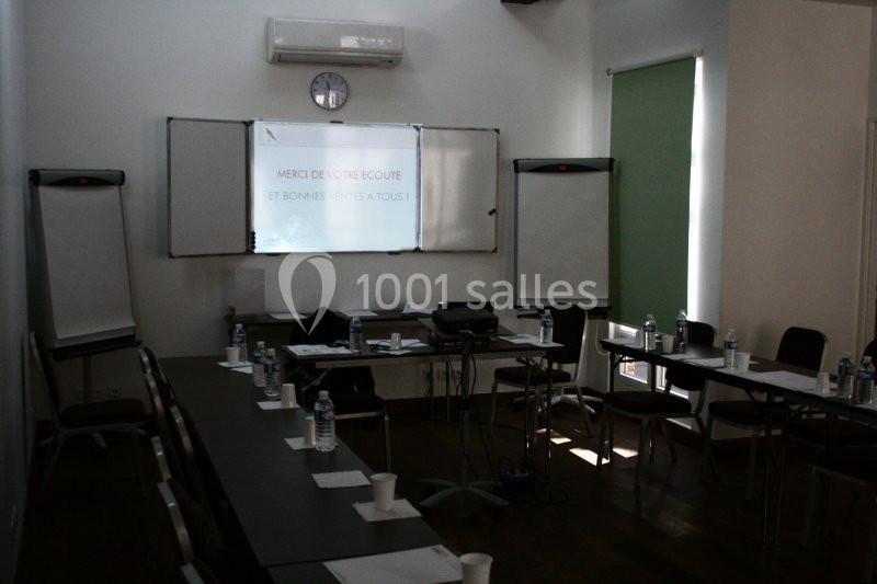 Salle de réunion sombre avec tables, chaises, paperboards, bouteilles d'eau et un projecteur affichant un message.