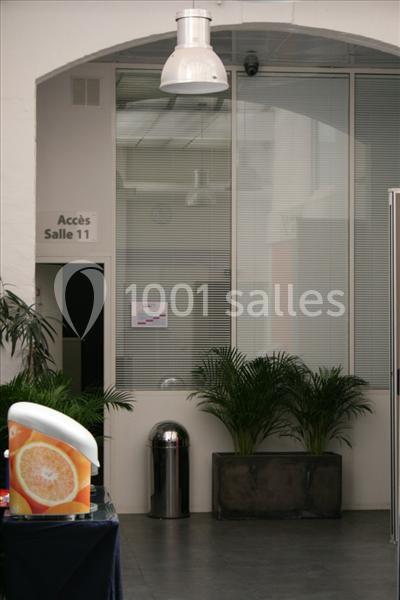 Accès à une salle identifié comme ’Salle 11’, avec plantes, poubelle métallique et distributeur en premier plan.