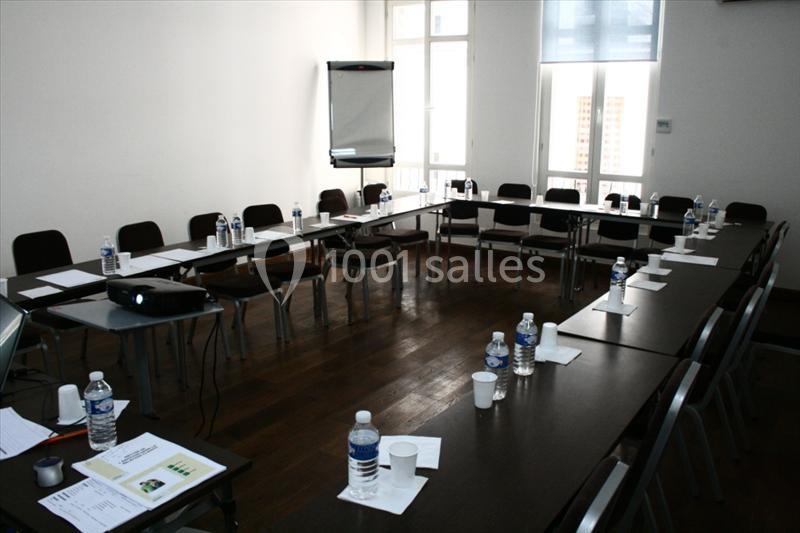 Salle de réunion en U avec tables, chaises, bouteilles d'eau, gobelets et matériel de présentation.