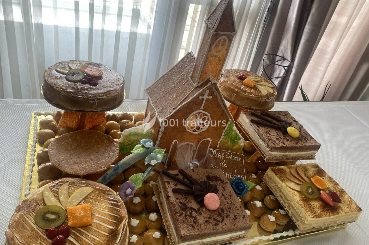 Pièce montée en pâte à choux et gâteaux décorés, avec une église en sucre pour un baptême, sur une table blanche.