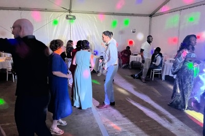Des personnes dansent sous des lumières colorées dans une grande tente lors d'un événement festif.