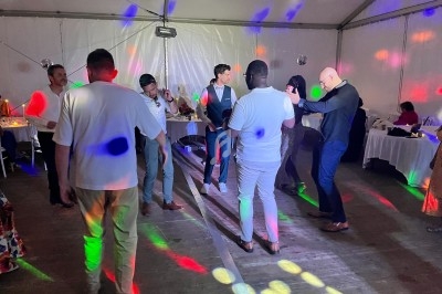 Des personnes dansent sous des lumières colorées dans une salle avec des tables dressées en arrière-plan.