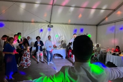 Des personnes dansent et discutent sous une tente éclairée par des lumières colorées lors d'un événement festif.